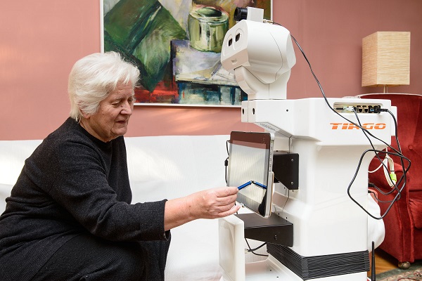 An Image Dpicting The Concept Of Cobots Helping Elders - An Old Lady Operating Collaborative Robot From Her Home.